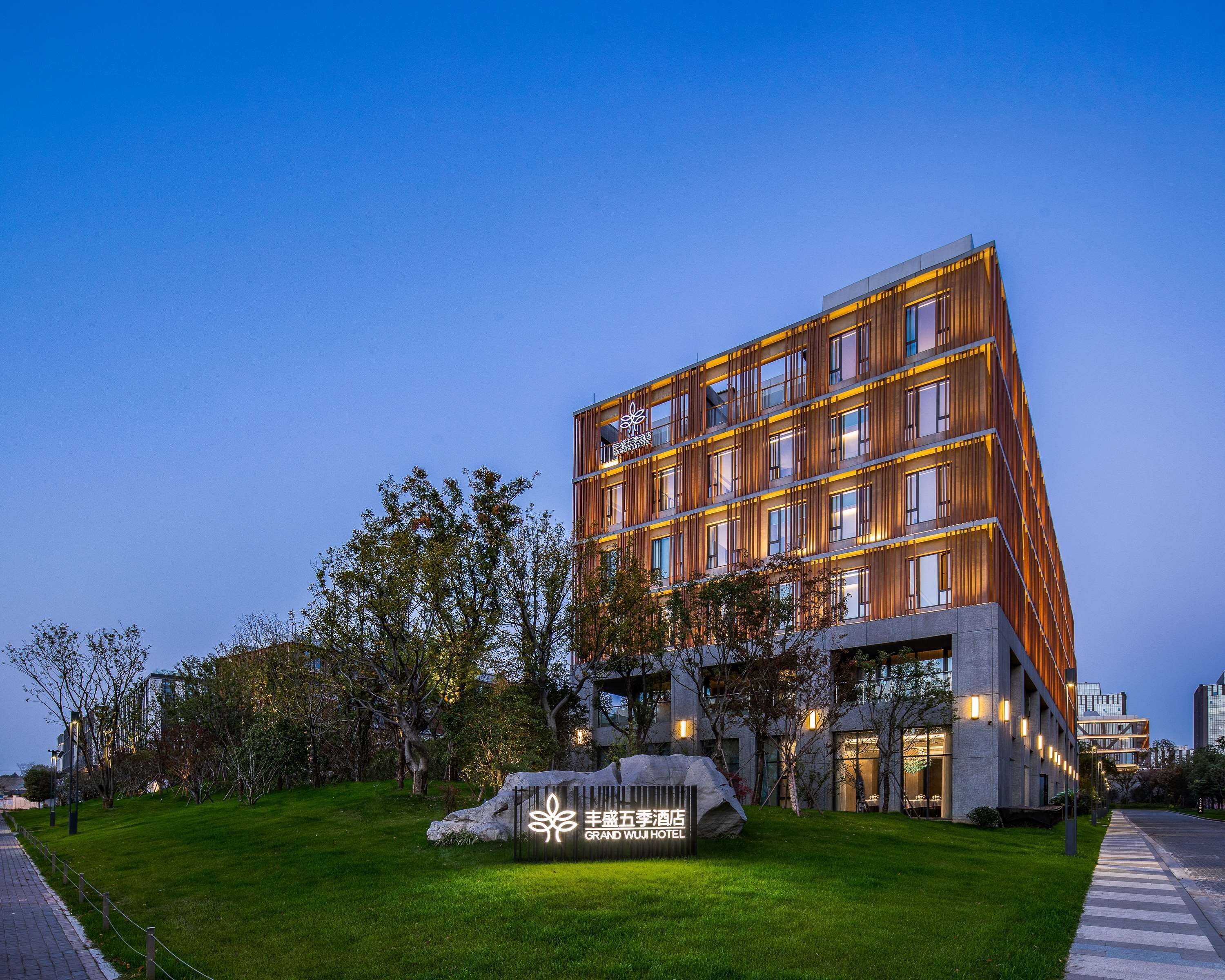 Un hôtel moderne, reconnaissable à son enseigne bien visible à l’entrée, entouré d’un espace verdoyant bien entretenu et bordé d’un chemin pavé.