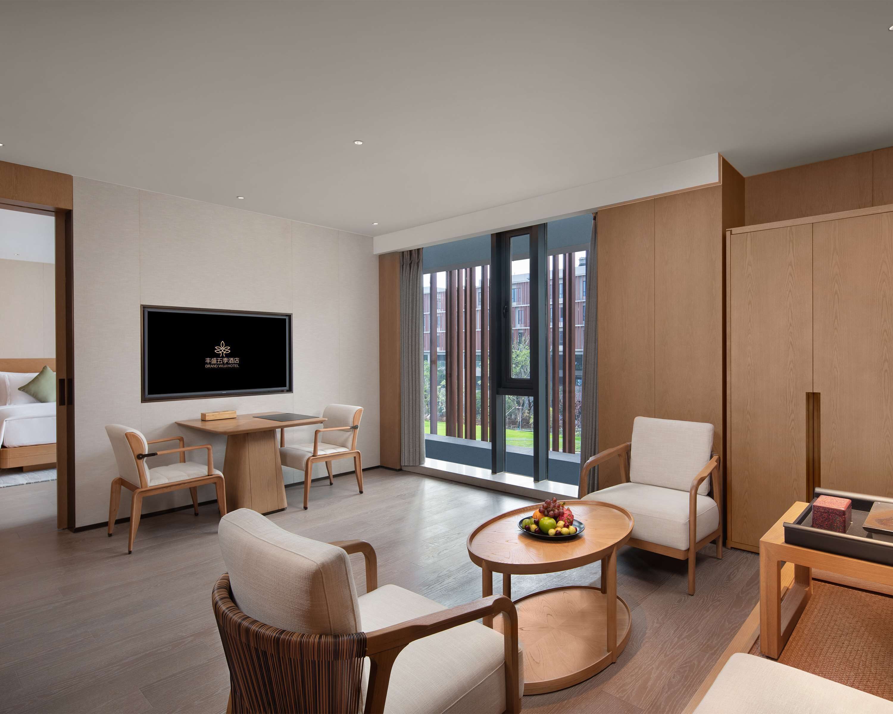 Ein modernes Hotelzimmer mit großem Fernseher, bequemen Sitzgelegenheiten, einem Essbereich und einem Balkon mit Blick.