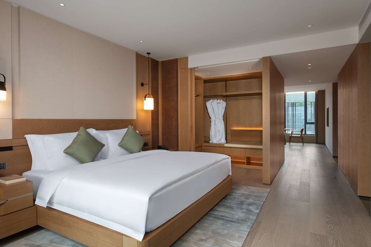 Habitación de hotel moderna con una cama grande, cabecera de madera, mesitas de noche, un vestidor amplio y vistas al exterior.