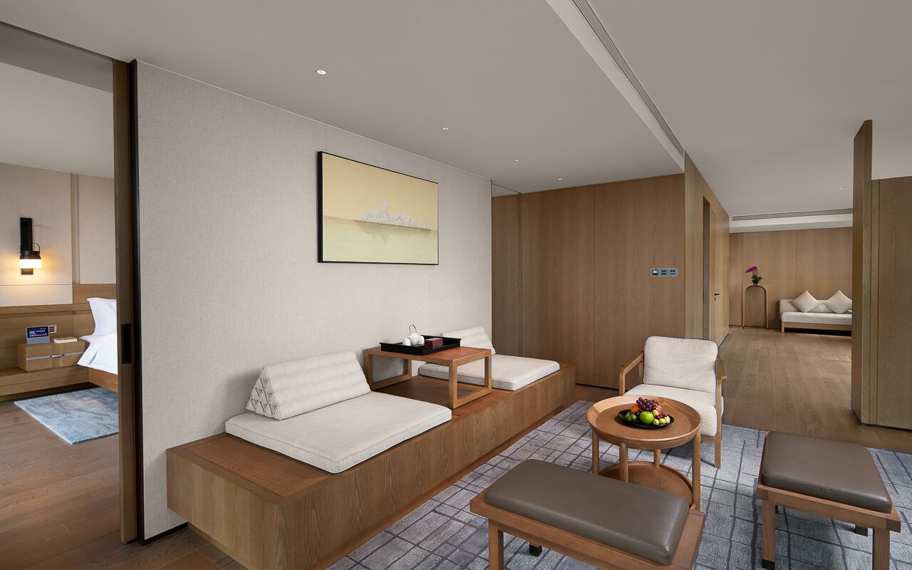 Une chambre d’hôtel moderne avec un canapé, une petite table sur laquelle sont disposés des fruits, une chaise et un lit avec une table de chevet.
