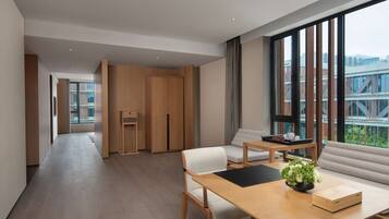 Una habitación de hotel moderna con suelo de madera, un ventanal con vistas a la ciudad, un escritorio de madera con una planta y un sofá.