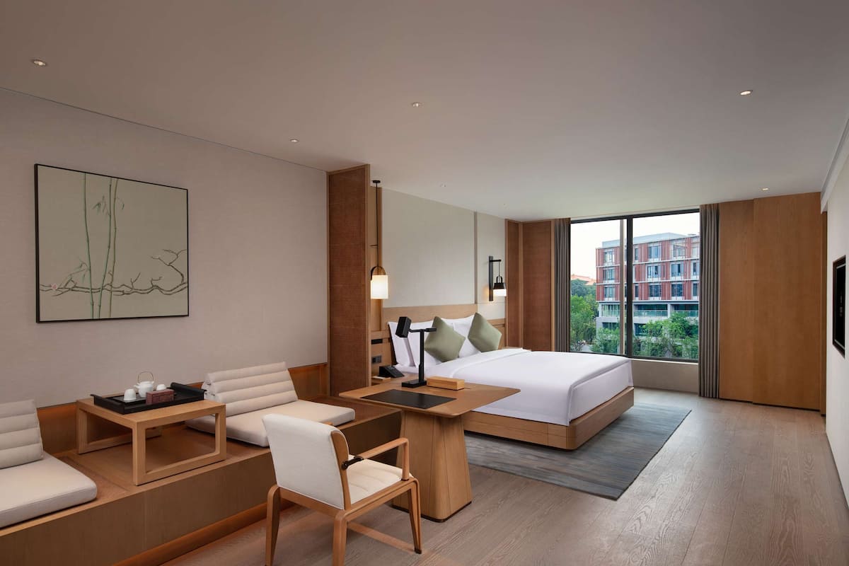 Habitación de hotel moderna con cama, escritorio, silla y un gran ventanal con vistas a edificios.