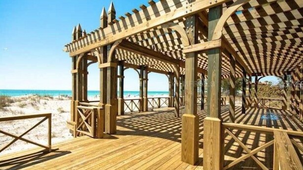 Een houten strandpaviljoen met een geruit dak en open zijkanten, met uitzicht op het strand.