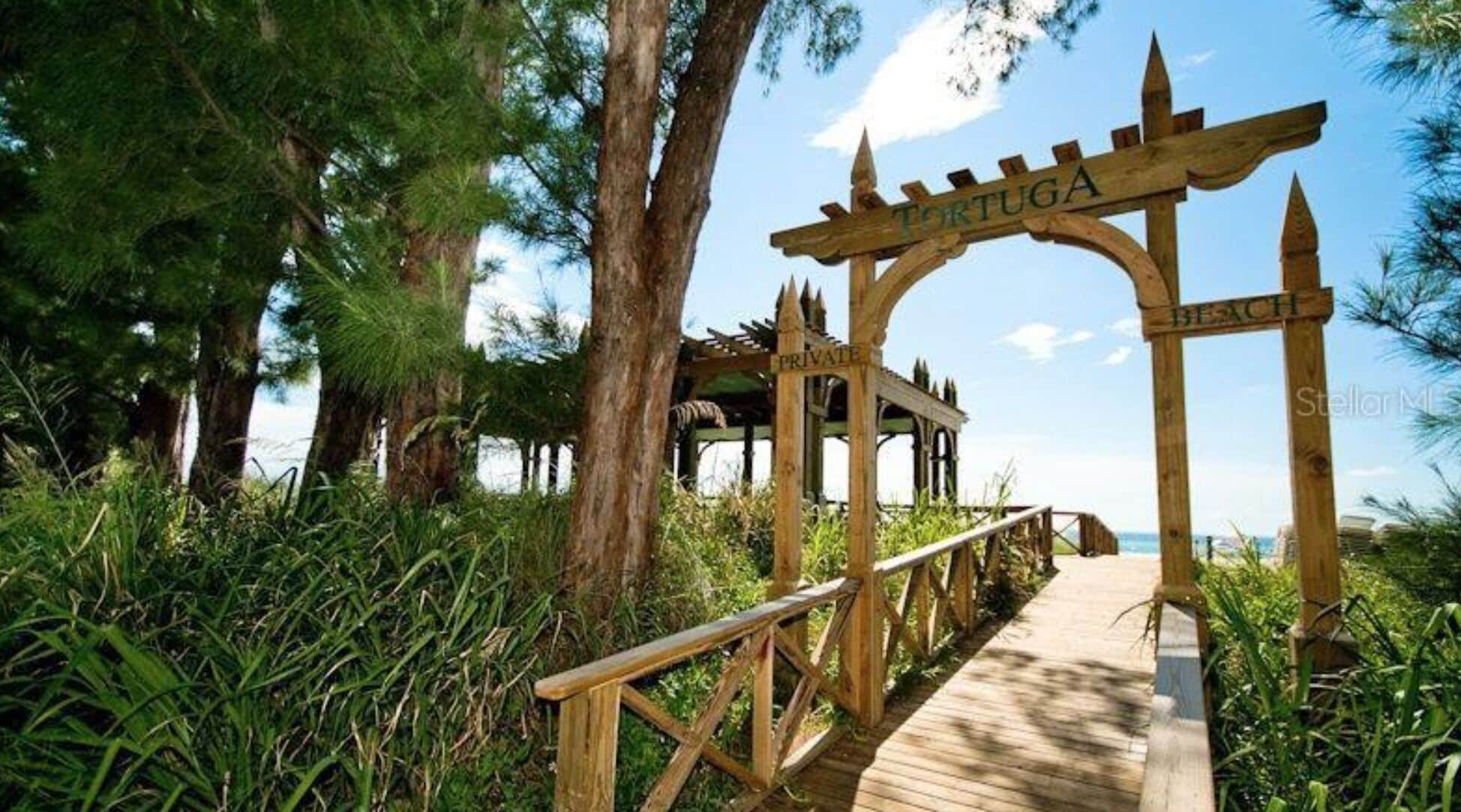 A wooden pathway leading to a private beach area with a sign reading "TORTUGA BEACH".