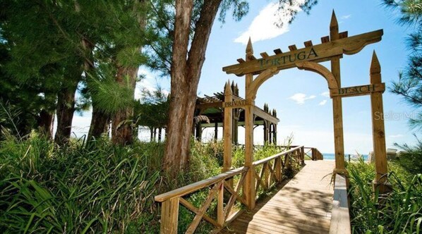 A wooden pathway leading to a private beach area with a sign reading "TORTUGA BEACH".