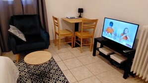 Ein Wohnzimmer mit einer schwarzen Couch, einem kleinen runden Tisch, einem Fernseher und einem Holzessttisch mit Stühlen.