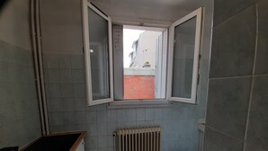 Eine kleine Küche mit Fenster, Heizkörper und Mülleimer.