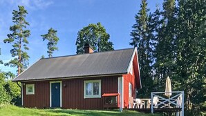 A small, single-story wooden house with a dark roof, a red door, and a small porch area.