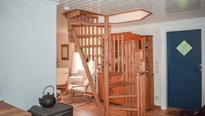 A room with a wooden staircase, a door with a window, a small table with a lamp, and a vintage stove.