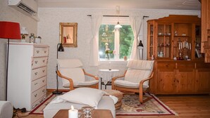 A cozy room with a wooden cabinet, two chairs, a small table with a candle, and a window with curtains.