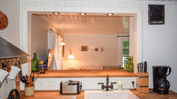 A kitchen with a large sink, a mirror above the counter, and a window with curtains.
