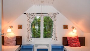 A bedroom with two beds, a window with floral curtains, and wall-mounted lamps.