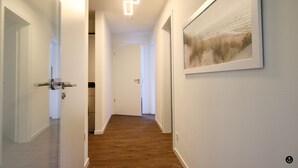 A hallway with wooden flooring, white walls, and a framed landscape painting. - Refugium 2 (Kellenhusen)