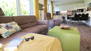 A modern living room with a brown sofa, a green ottoman, and a dining area with black chairs. - Refugium 2 (Kellenhusen)