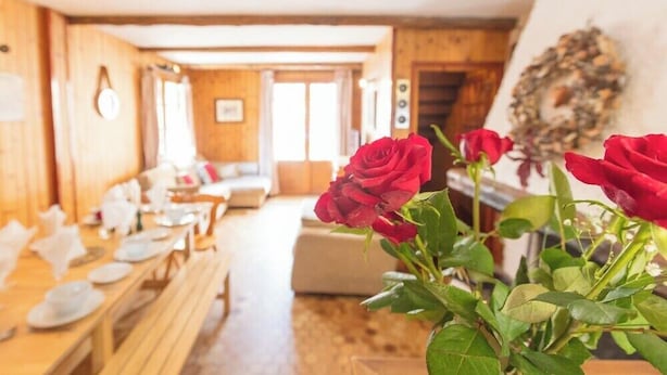 A wooden interior with a dining area, a sofa, and a vase with red roses.