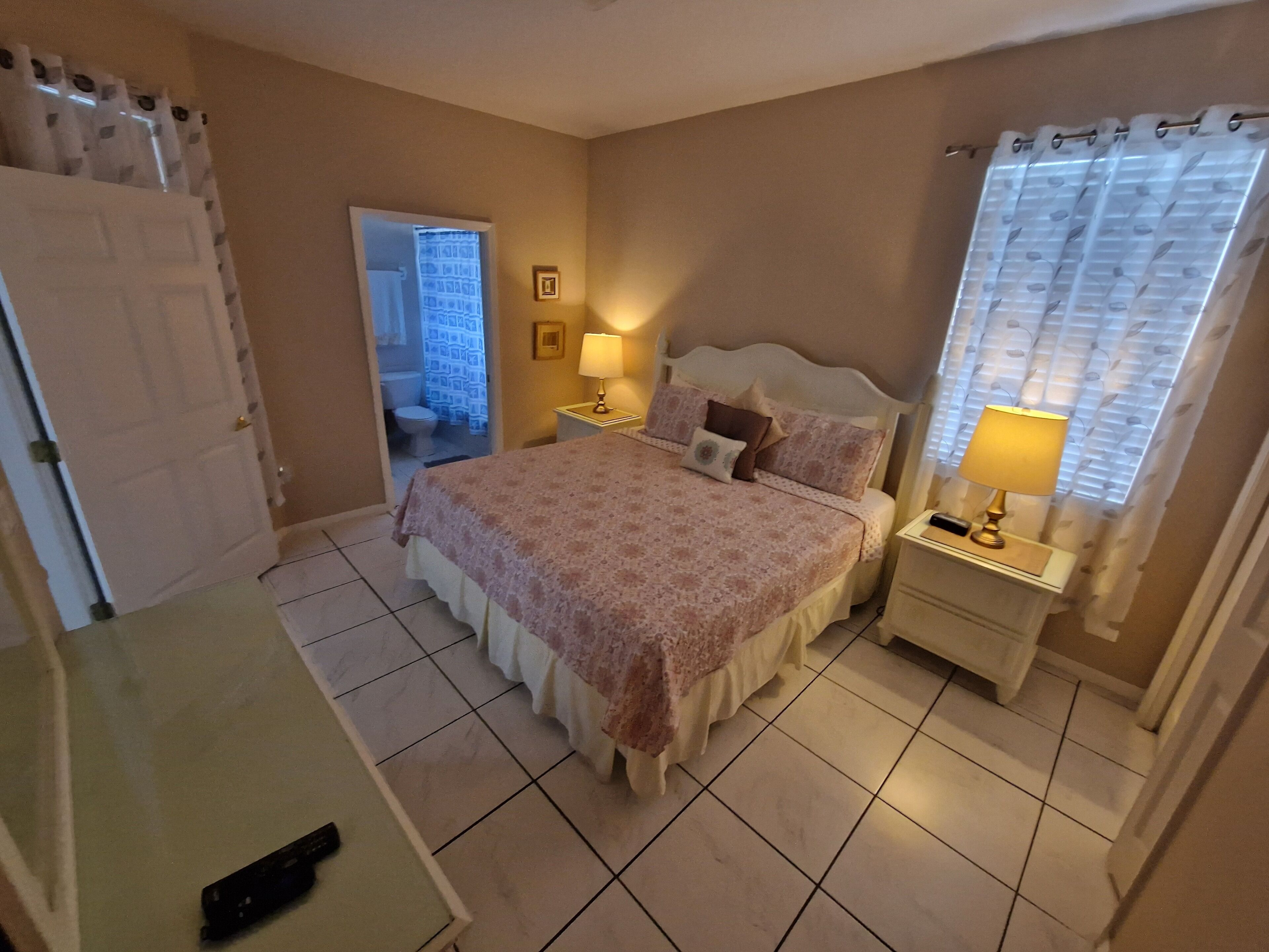 Camera da letto con un letto, comodini, un tavolino e un bagno visibile attraverso una porta aperta.