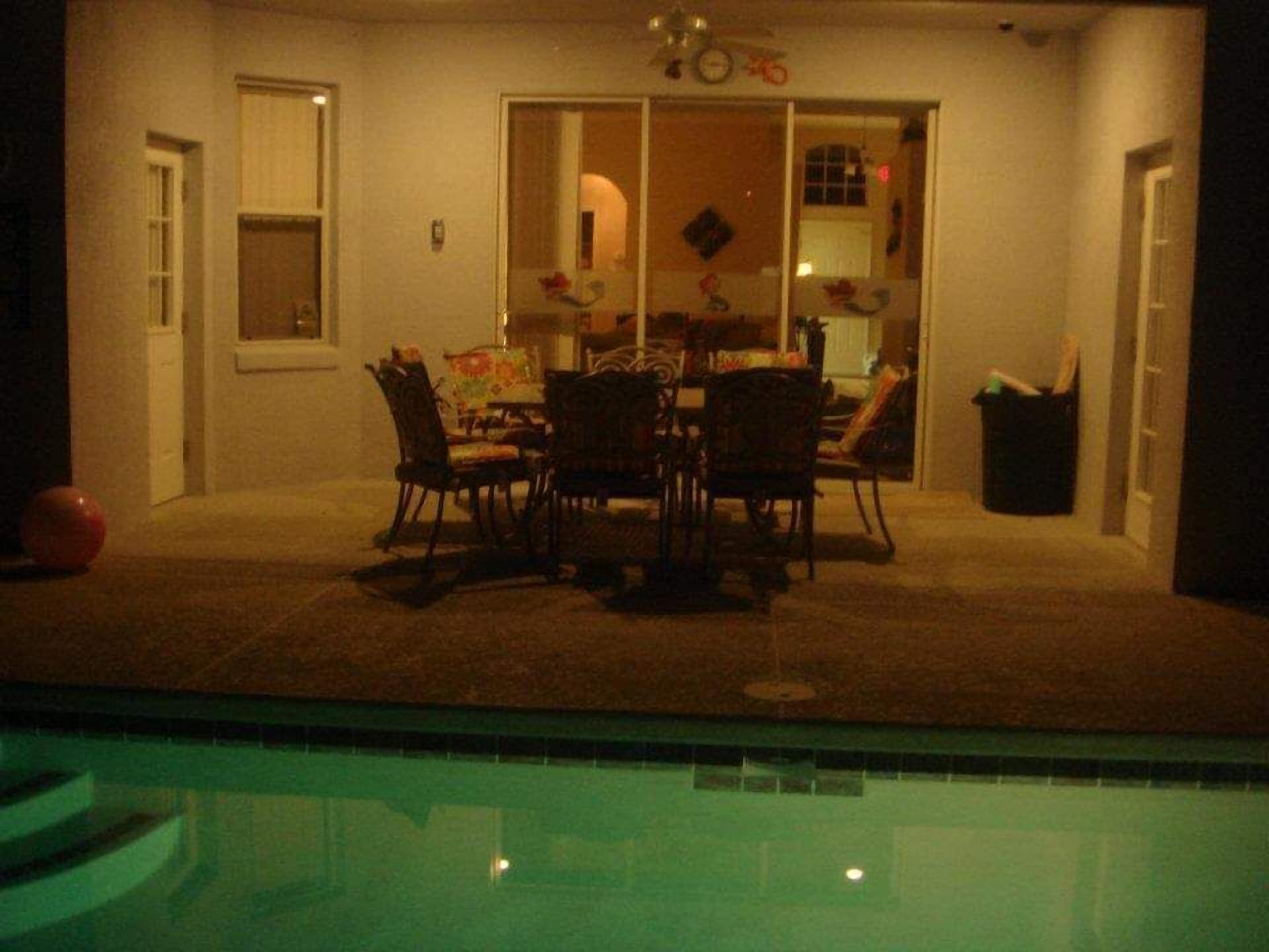 A poolside area with a dining table and chairs, a trash bin, and a window.
