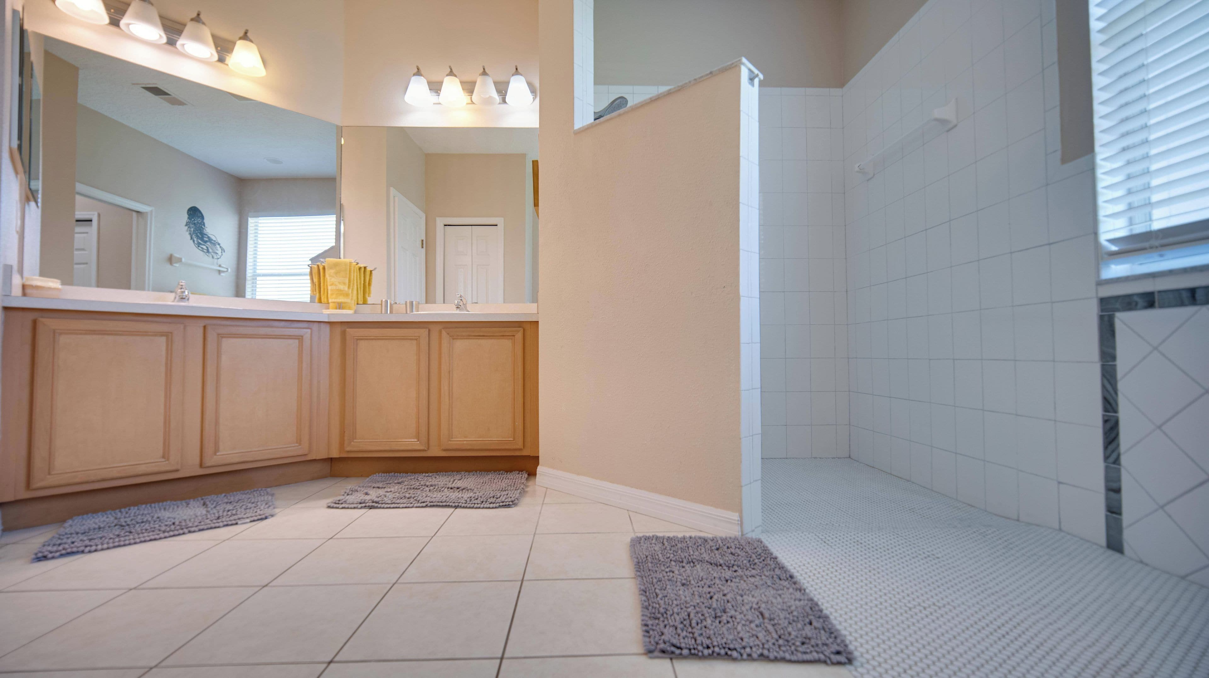 A bathroom with a shower, a sink with a mirror, and two rugs on the floor.