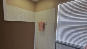 Ein Badezimmer mit Dusche, Handtuchhalter mit Handtuch, einem Fenster mit Jalousien und einem Fliesenboden.