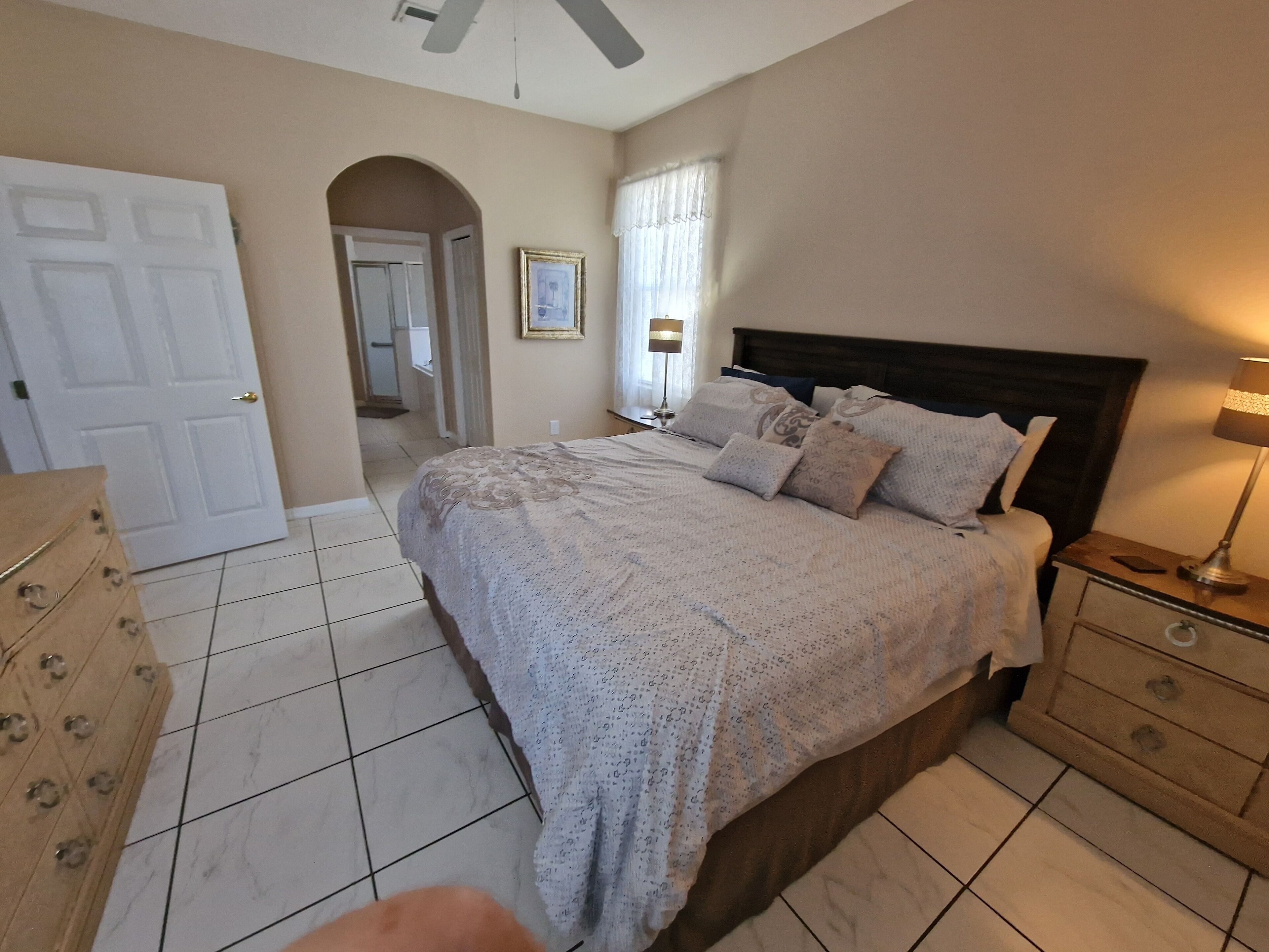 A bedroom with a bed, nightstand, dresser, and a door leading to another room.