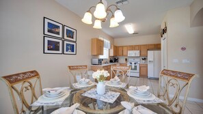 A dining area with a glass table surrounded by chairs, a vase with flowers, and framed pictures on the wall.