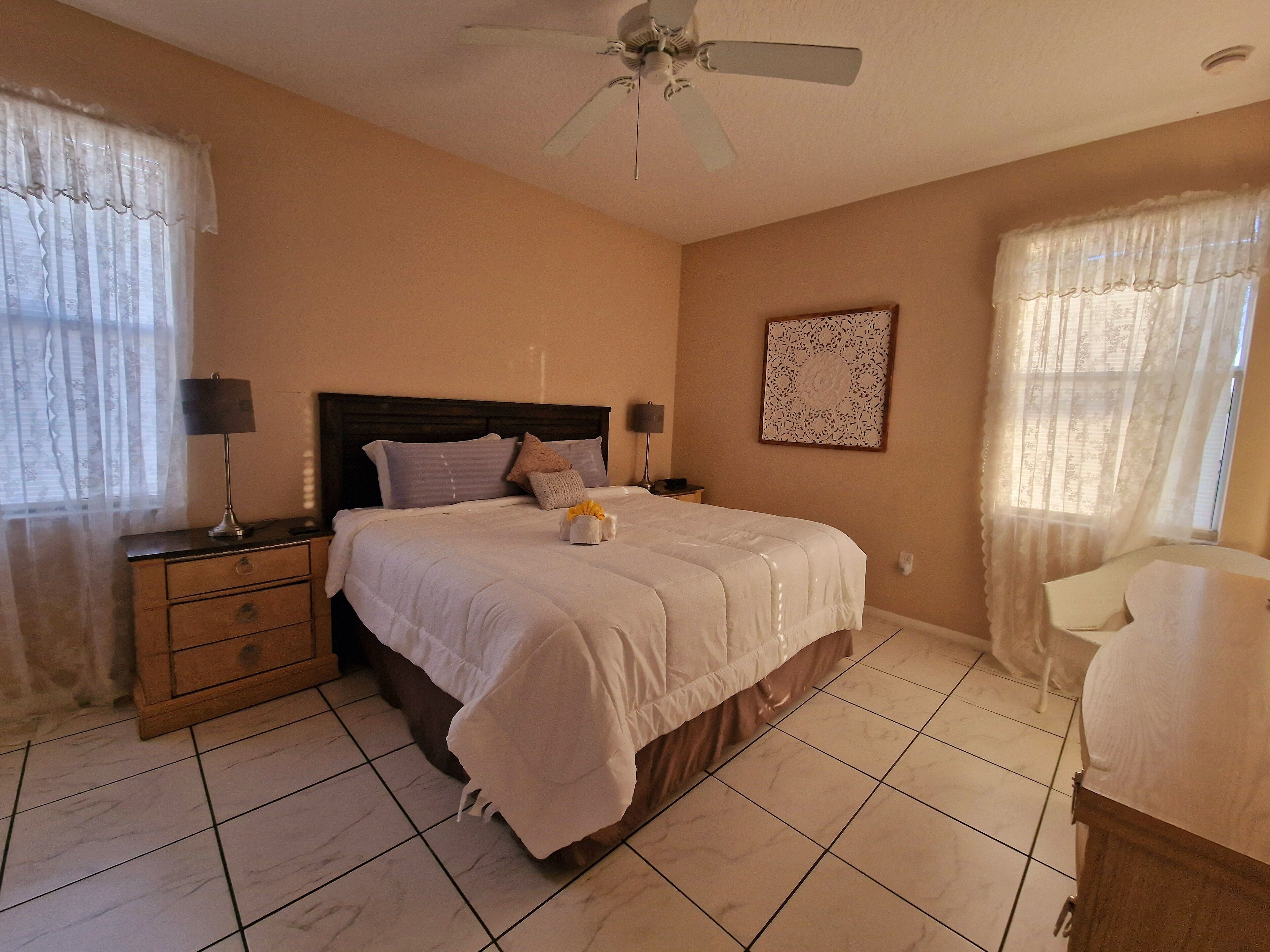 A bedroom with a bed, nightstands, a ceiling fan, and a wall-mounted artwork.