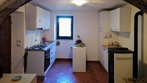 A compact kitchen with a gas stove, a small refrigerator, and a window. - Casa nel Borgo di Santa Fiora (Santa Fiora)