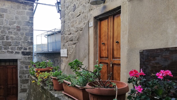 A narrow alley with a stone building, wooden door, and potted plants. - Casa nel Borgo di Santa Fiora (Santa Fiora)