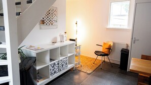 A compact living space with a staircase, a white shelving unit, a radiator, a small table, and a window.