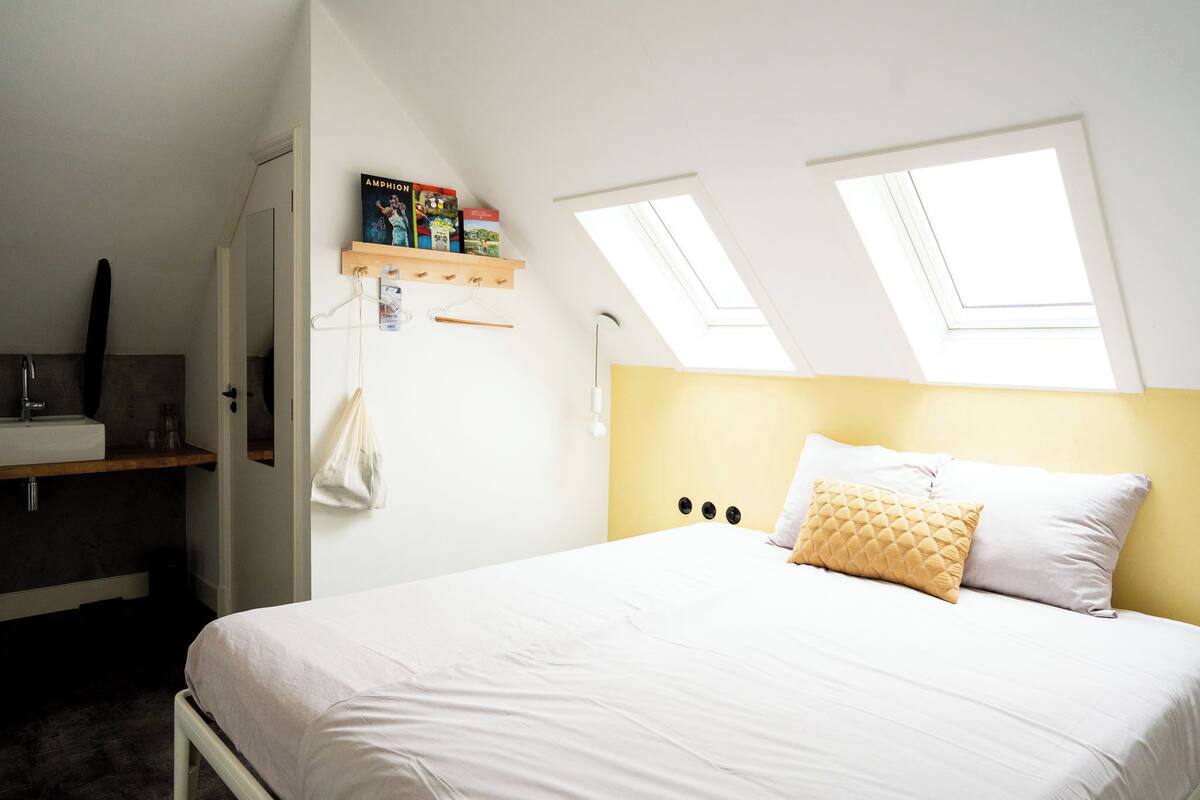 Un dormitorio con cama, mesita de noche, toalla colgada y tragaluz.