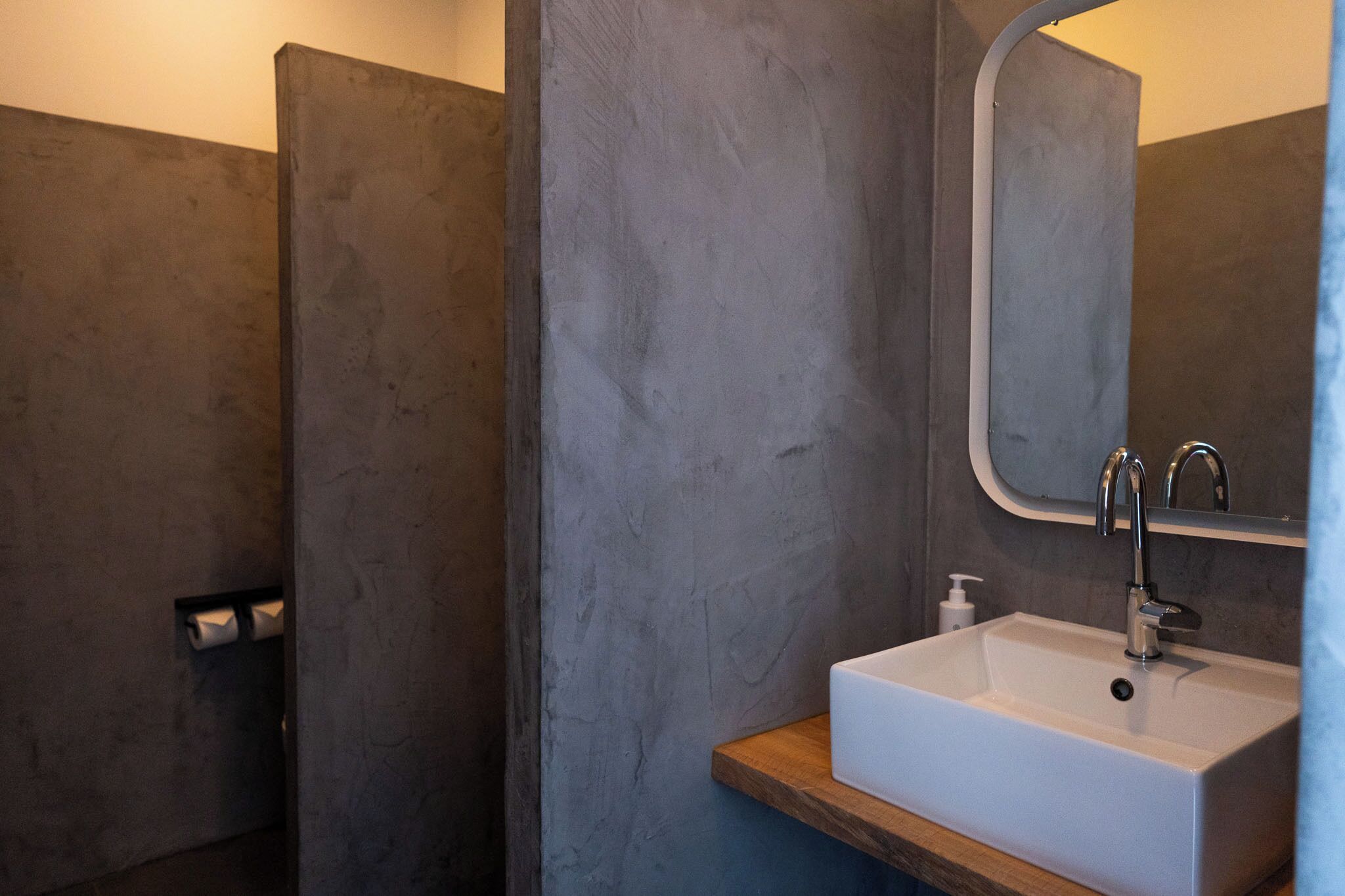 A bathroom with a white sink, a mirror, and a wooden shelf.