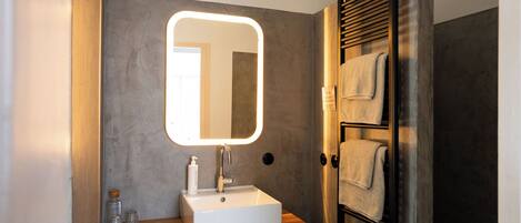 A modern bathroom with a large mirror, a white sink, and a towel rack.