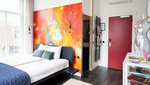 A modern bedroom with a large bed, a vibrant abstract wall, a red door, and a mannequin with jewelry.