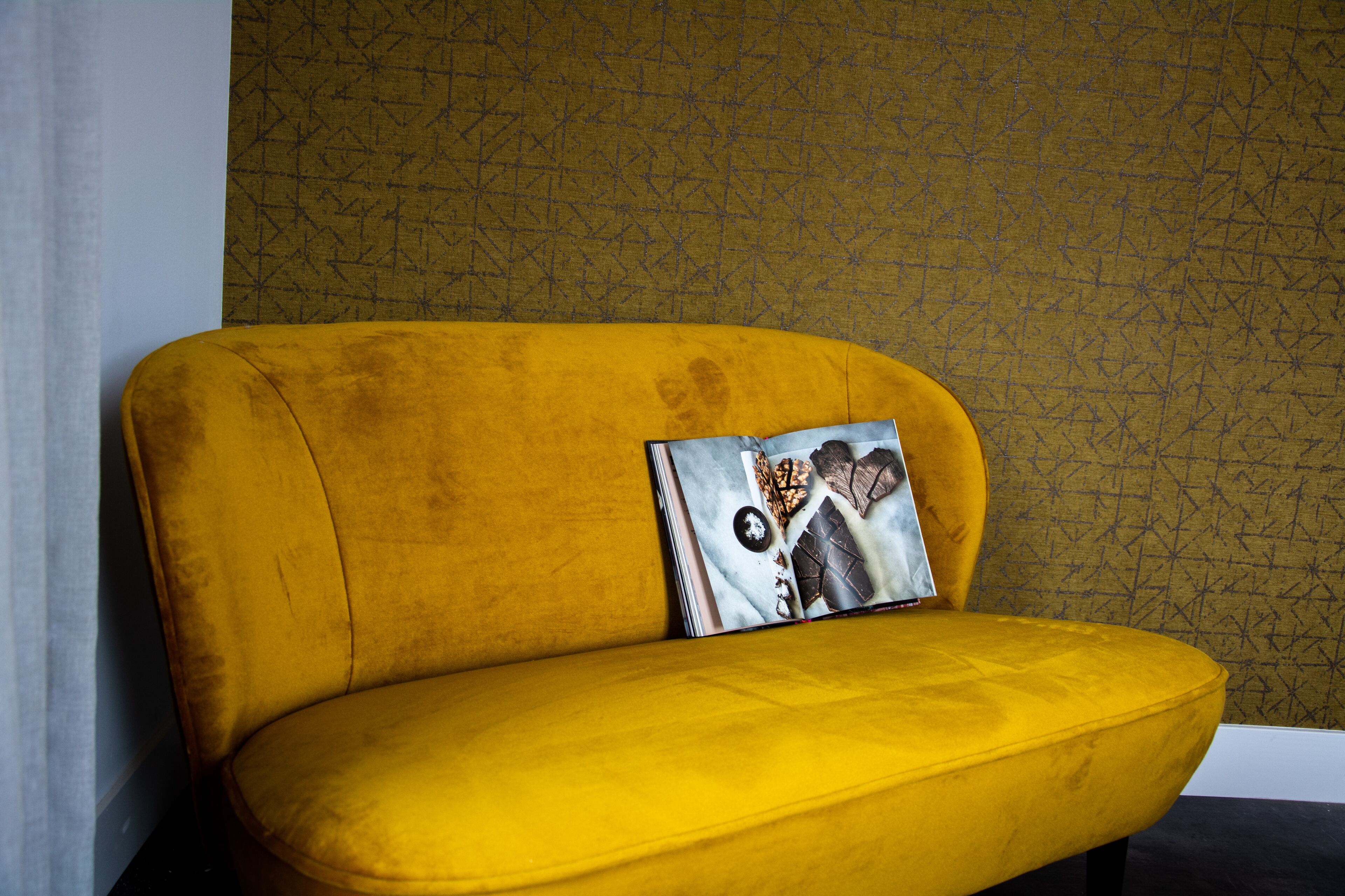A yellow sofa with a patterned cushion against a textured wall.