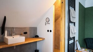 A modern bathroom with a white sink, wooden shelf, and a towel rack.