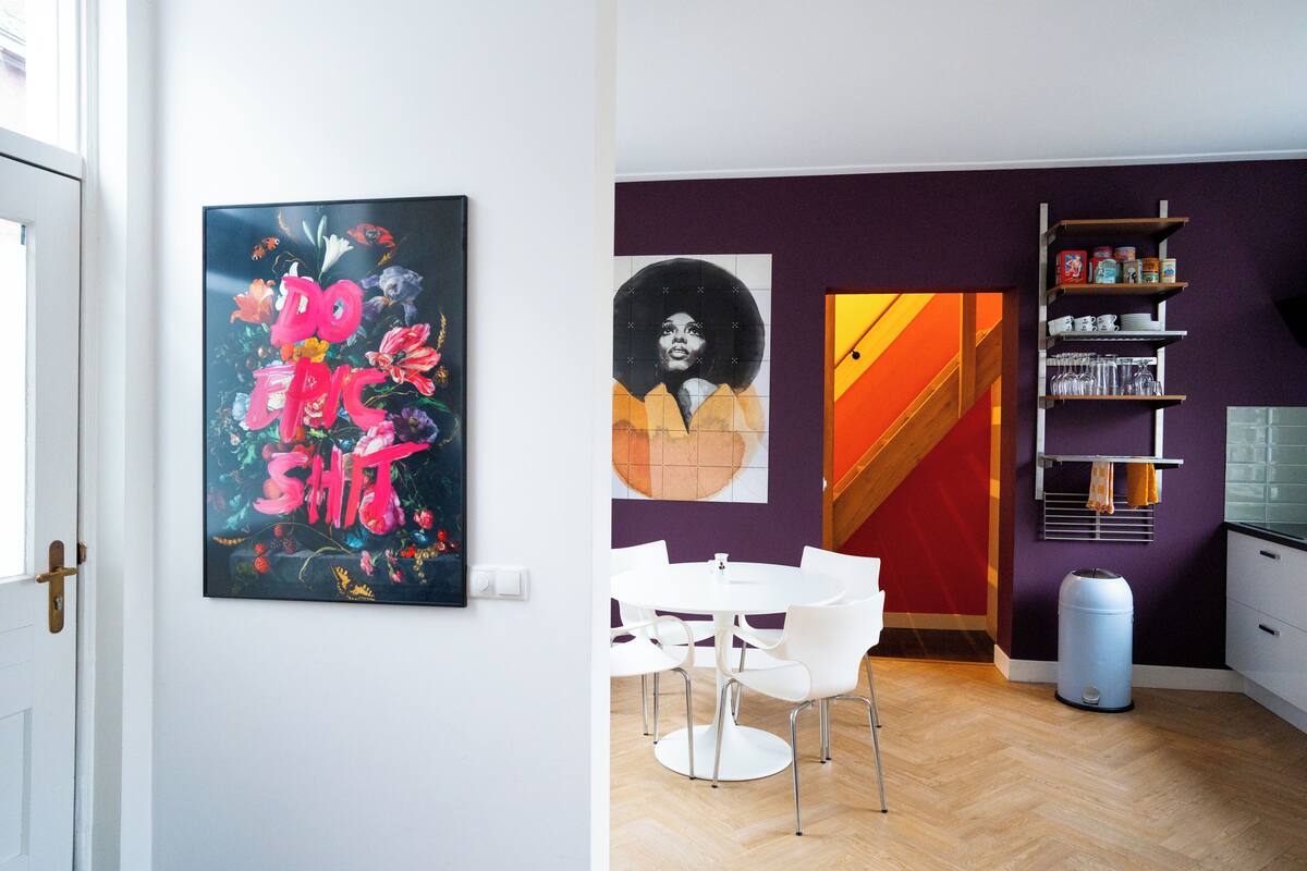 Una cocina moderna con armarios blancos, una pared de acento morada y un comedor con sillas blancas.