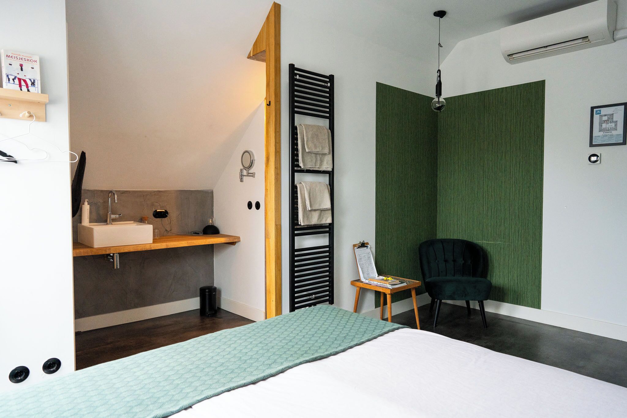 Una camera da letto moderna con un letto, una toeletta con lavandino, un portascopevoli, una sedia e una parete verde decorativa.