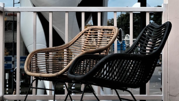 Two wicker chairs on a wooden deck with a modern white structure in the background.