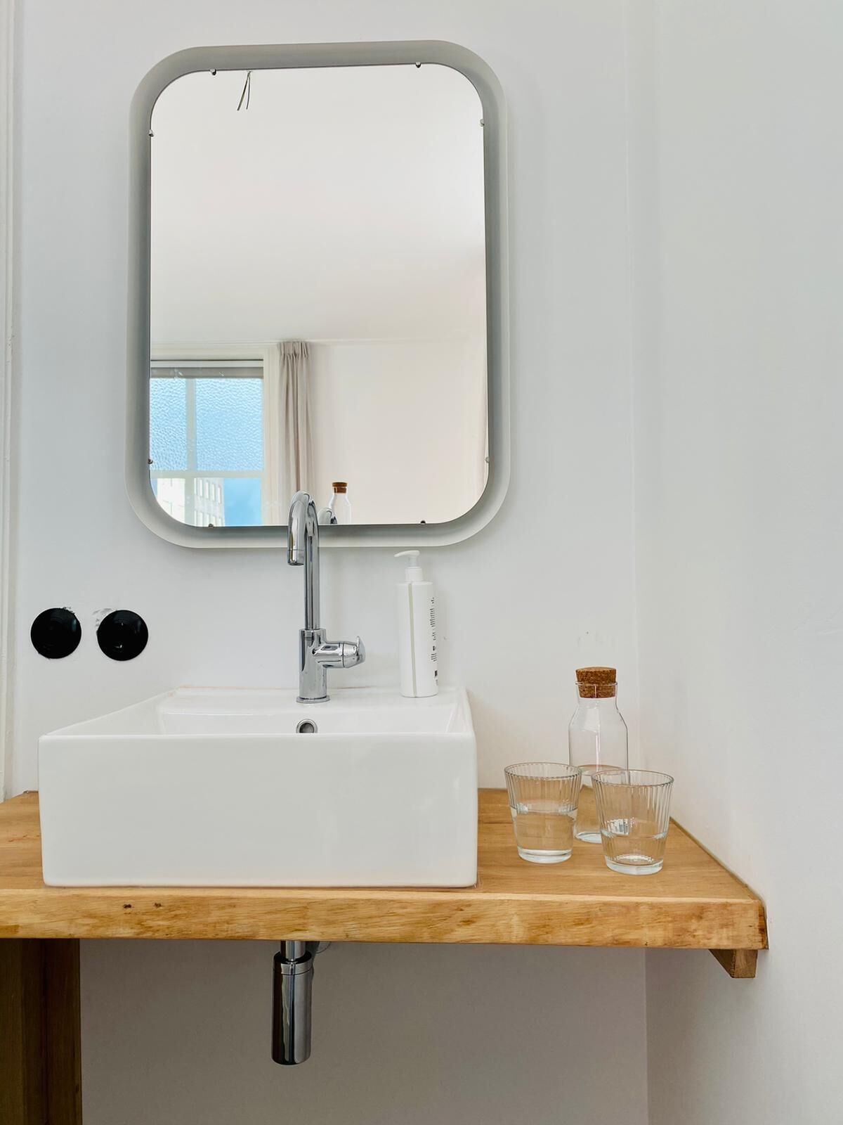 Ein weißes Waschbecken mit einem rechteckigen Spiegel darüber.