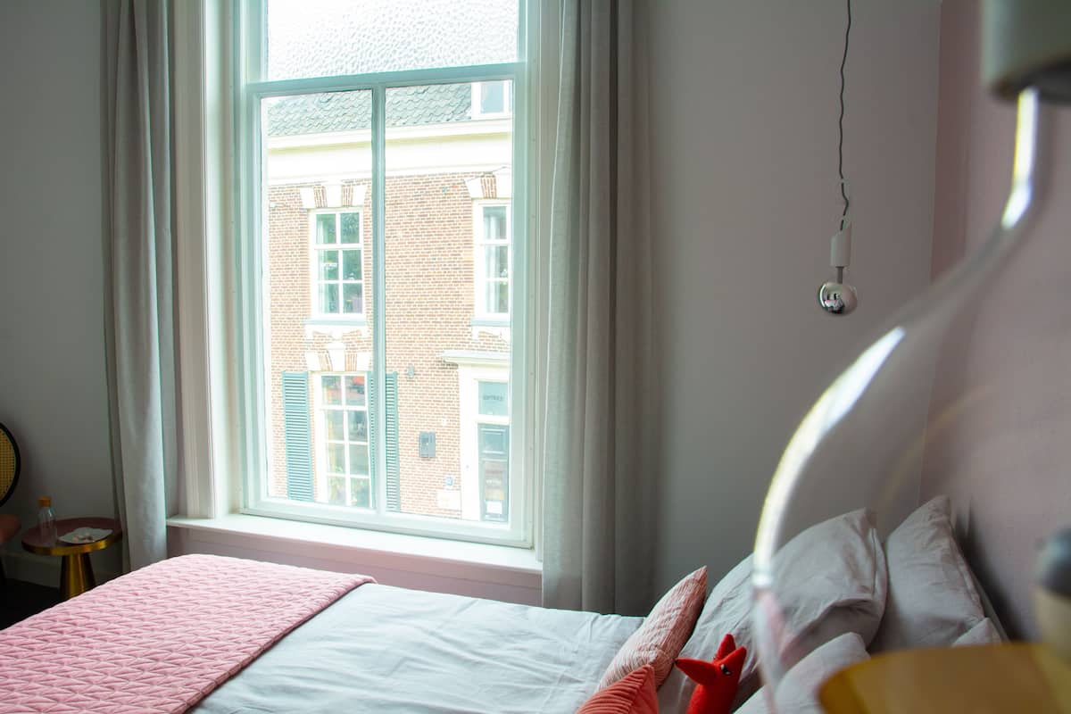 Un dormitorio con cama, ventana y vista a un edificio de ladrillo.