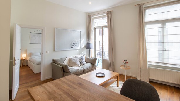 A modern living room with a wooden dining table, a sofa, and a small side table with a lamp. - Comfortable 1 bedroom - Fully equipped kitchen - Brussels center (Bruxelles)