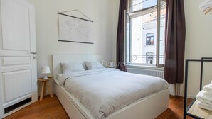 A bedroom with a bed, a window with curtains, a radiator, and a map on the wall. - Comfortable 1 bedroom - Fully equipped kitchen - Brussels center (Bruxelles)