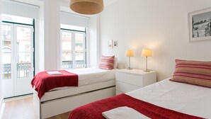 Un dormitorio con dos camas, una ventana, una puerta y una lámpara fijada a la pared.