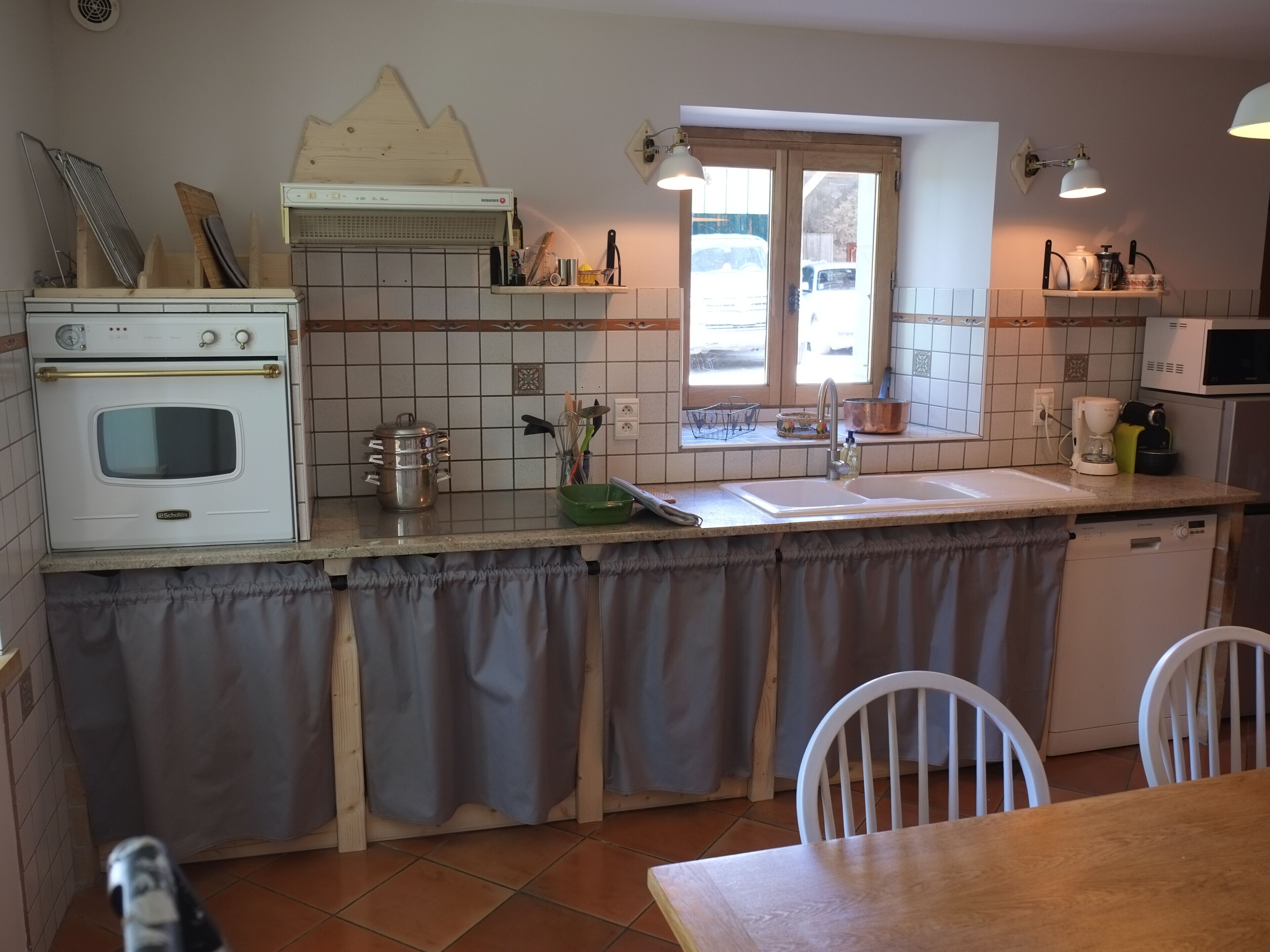 A kitchen with a double oven, a sink, a window, and a dining area with chairs.