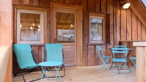 Une cabane en bois avec une véranda, deux chaises pliantes, une petite table et de grandes fenêtres.