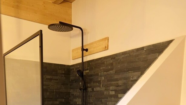 Une douche moderne avec une porte en verre, des carreaux de pierre foncée et une étagère en bois.