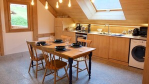 Une cuisine avec des meubles en bois, une table à manger avec des chaises, un lave-linge et une lucarne.