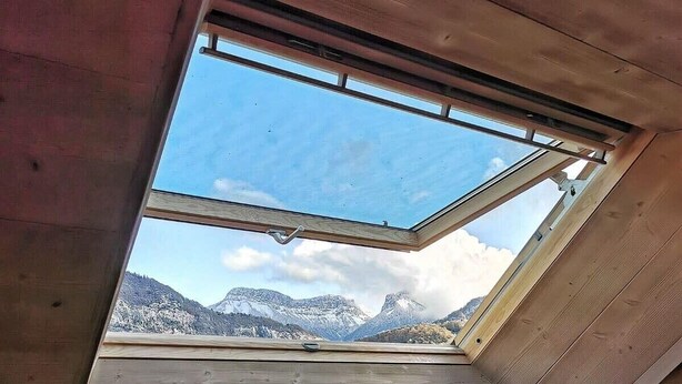 Une lucarne dans une cabane offrant une vue sur des montagnes enneigées.