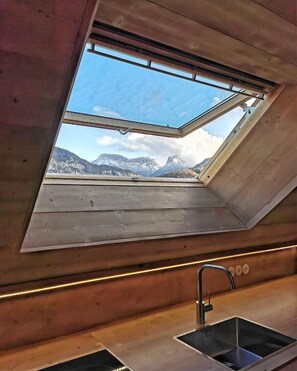 Une lucarne dans une cabane offrant une vue sur des montagnes enneigées.