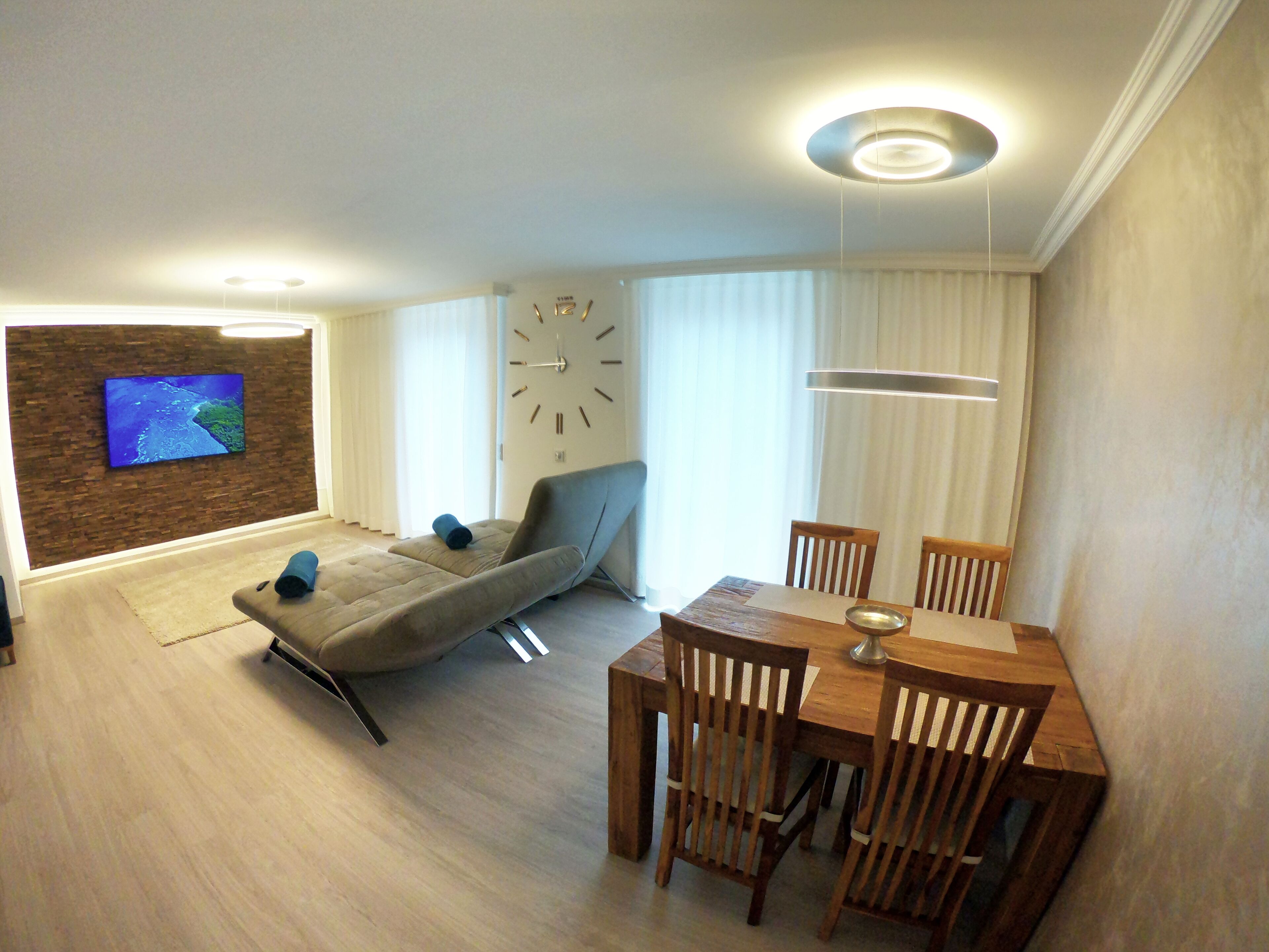 Ein modernes Wohnzimmer mit einer Couch, einem Esstisch und einem an einer Ziegelwand montierten Fernseher.